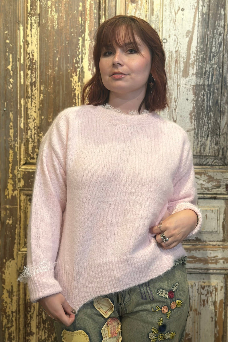 Person wearing a light pink sweater and patchwork jeans against a wooden background